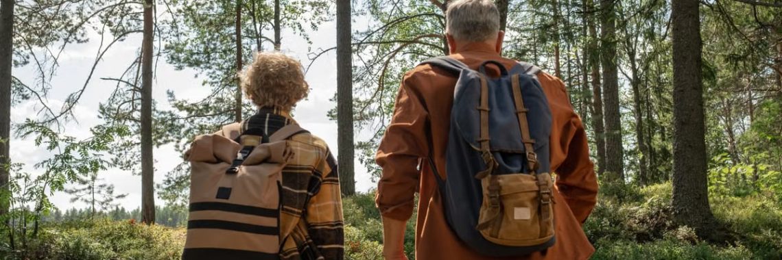 A grandfather and grandson enjoy a bonding hike through a sunlit forest with backpacks.